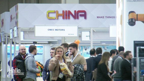 Vista attraverso un corridoio di una fiera con molti visitatori e una piattaforma con un'iscrizione "Cina".  © Schermata 