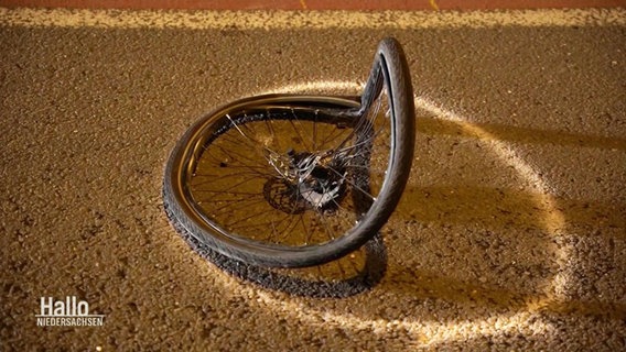 Auf Straßenasphalt liegt ein von Kreide umrandeter, verbeulter Fahrradreifen mitsamt Speichen. © Screenshot 