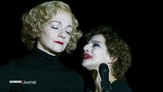 Zwei Schauspielerinnen, die Marlene Dietrisch und Edith Piaf verkörpern, nähern sich in einer Szene auf der Bühne an. © Screenshot 