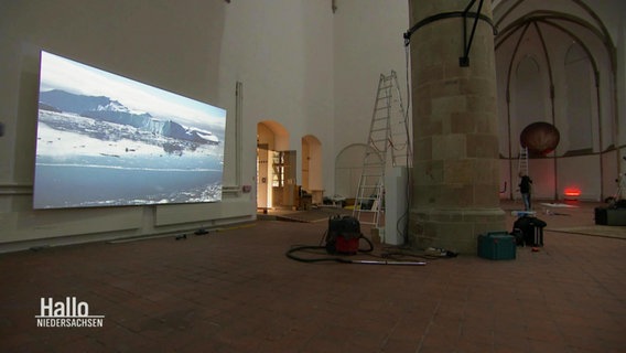 Eine große Halle wird für eine Kunstausstellung vorbereitet © Screenshot 