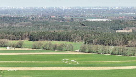 Ein Helikopter zieht an einem Seil eine kreisrunde Ring-Konstruktion hinter sich durch die Luft. © Screenshot 