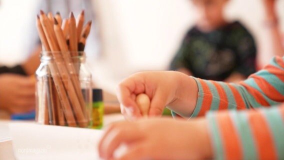Eine Kinderhand mit Kreide zwischen den Fingern über einem Tisch © Screenshot 