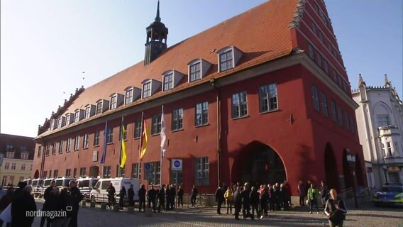 Ein rotes Gebäude mit Fahnen oben drauf, von außen ist die Fassade zu sehen © Screenshot 