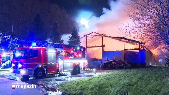 Ein Feuerwehrauto steht neben einer brennenden Halle. © Screenshot 