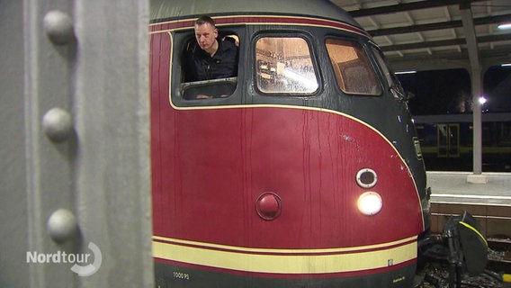 Der Zugführer des nostalgischen Zuges "Eierkopf" schaut aus der Kabine heraus. © Screenshot 