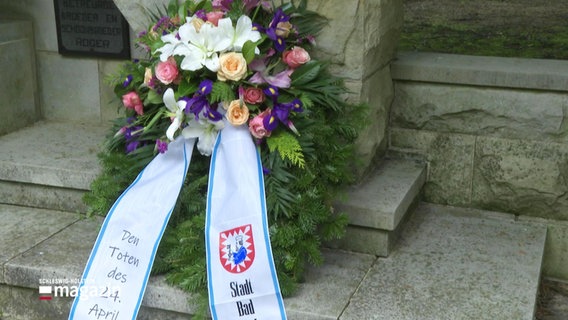 Ein Blumengesteck lehnt an einem Denkmal für die Opfer des Zweiten Weltkrieges. © Screenshot 
