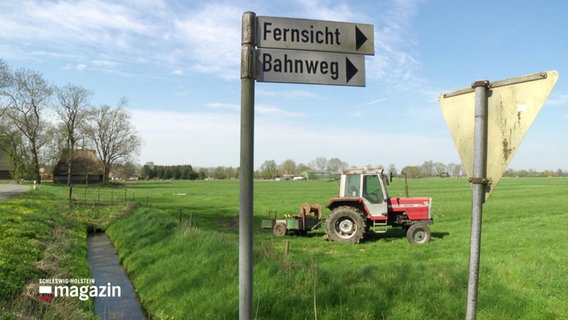 Wegweiser in der kleinen Dorfgemeinde Moorhusen weisen zu den Wegen Fernsicht und Bahnweg, im Hintergrund ein Trecker. © Screenshot 