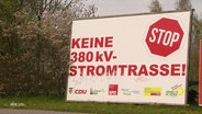 An einer Straße steht ein großes Schild mit der Aufschrift: "Keine 380kV-Stromstrasse!" © Screenshot 