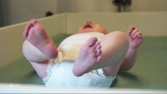 Ein Säugling liegt auf dem Rücken auf einem Untersuchungstisch. © Screenshot 