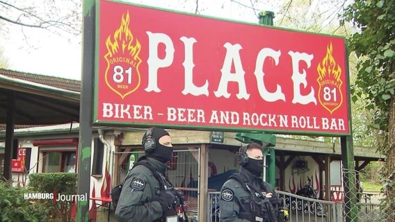Zwei Polizisten stehen bei einer Razzia vor einer Hells Angels Bar. © Screenshot 