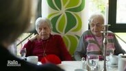 Zwei Seniorinnen sitzen nebeneinander an einem Tisch. © Screenshot 