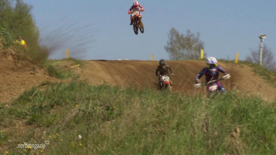 Ein Motocross ist in der Luft und zwei weitere fahren auf einer hügeligen Strecke vorweg. © Screenshot 