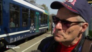 Ein Mann steht neben einem Zug und gibt ein Interview. © Screenshot 