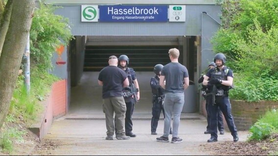 Mehrere Einsatzkräfte der Polizei stehen in gut geschützter Uniform vor einem Eingang zu einer S-Bahn-Station. © Screenshot 