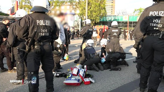 Polizeibeamte kümmern sich um eine am Boden liegende Person. Daneben liegt Material für eine Notfallversorgung im Erste-Hilfe-Fall. © Screenshot 