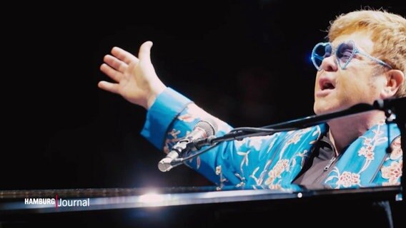 Elton John singt und spielt an einem Klavier. Er trägt einen auffälligen blauen Anzug und eine dazu passende blaue Brille. © Screenshot 
