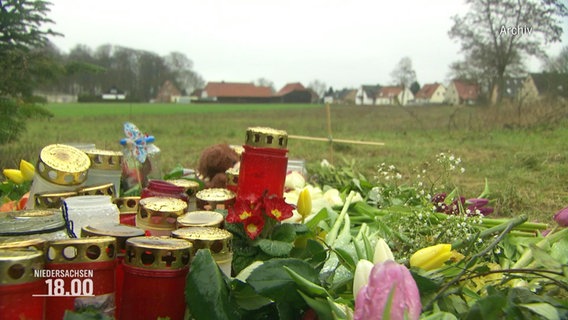 Nahaufnahme einer Gedenkstätte mit Grabkerzen und Blumensträußen auf einer Wiese © Screenshot 
