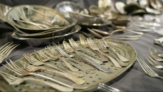 Viele Silber-Gabeln und Silber-Geschirr sind auf einer grauen Tischdecke ausgebreitet. © Screenshot 