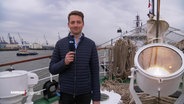Reporter Simon Ritter steht auf dem Deck eines Schiffes beim Hamburger Hafengeburtstag und blickt in die Kamera. © Screenshot 