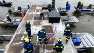 Mehrere Menschen in den Anzügen des THW arbeiten auf einem Ponton auf dem Wasser. © Screenshot 