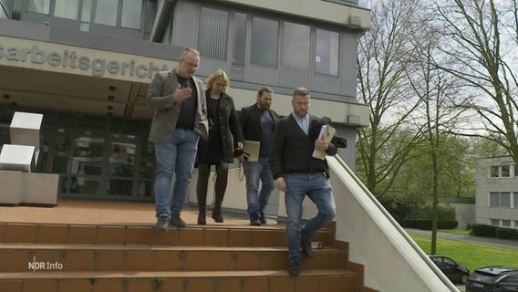 Vier Menschen gehen eine Treppe vor einem Arbeitsgerichtsgebäude hinunter. © Screenshot 