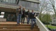 Vier Menschen gehen eine Treppe vor einem Arbeitsgerichtsgebäude hinunter. © Screenshot 