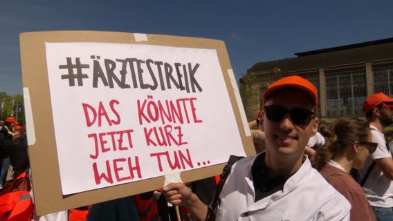 Ein Demonstrant mit einem Plakat mit der Aufschrift: "#Ärztestreik  Das könnte jetzt kurz weh tun...". © Screenshot 
