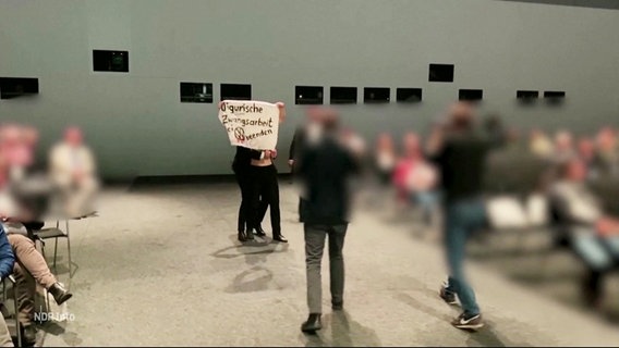 Aktivist:innen stürmen die Bühne bei einer Versammlung von VW-Aktionären. © Screenshot 