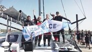Die Crew der Malizia Sea Explorer hält ein Banner zur feier des Zweiten Platzes. © Screenshot 