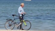 Ein Mann schiebt sein Fahrrad am Wasser entlang. © Screenshot 
