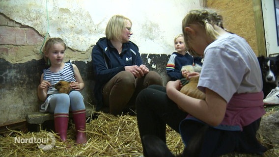 Nadine Tönjes sitzt mit mehreren Kindern auf dem Boden in einem Stall. © Screenshot 