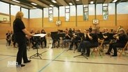 Das Orchester sitzt in einer Turnhalle. © Screenshot 