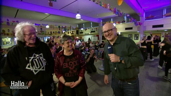 Ein NDR Reporter steht mit den Eltern von Niklas Kahl in einer Halle mit einigen Fans. © Screenshot 