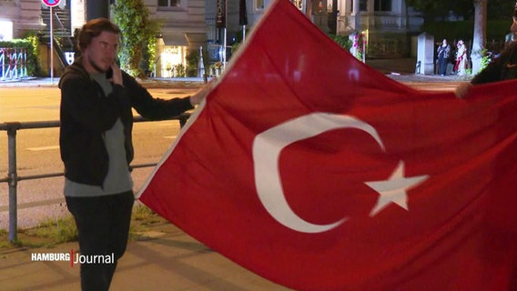 Junge Menschen breiten eine Türkei-Flagge auf einer Straße aus. © Screenshot 