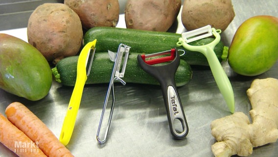 Vier Gemüseschäler liegen präsentiert und umgeben von Gemüse auf einer metallenen Arbeitsfläche. © Screenshot 