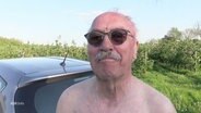 Ein älterer Herr mit Sonnenbrille und bloßem Oberkörper spricht in die Kamera. © Screenshot 