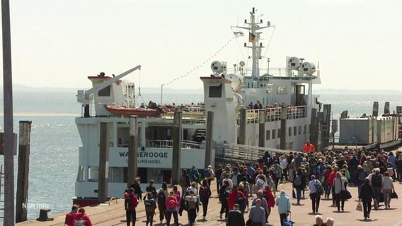 An einem Hafenkai strömen viele Fahrgäste auf ein kleineres Fährschiff zu. © Screenshot 
