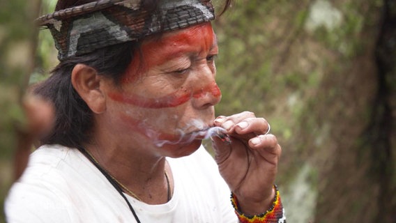 Ein Mann mit roter Gesichtsbemalung raucht an einem kleinen Zigarettenstummel. © Screenshot 