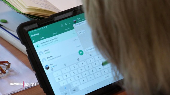 Ein Kopf einer Person sitzt vor einem Tablet mit einer geöffneten WhatsApp-Anwendung. © Screenshot 