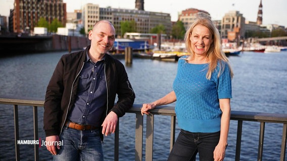 Die Moderatoren Maiken Nielsen und Ole Wackermann lächelnd auf einer Brücke über einem Fleet. © Screenshot 