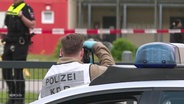 An einem Tatort fotografiert ein Beamter der Kriminaldauerdiensts die Situation im Hintergrund ist Polizeiabsperrband angebracht. © Screenshot 