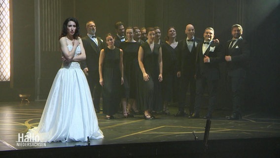 Szene aus "Semele": Sopranistin Marie Lys in einem langen, weißen Kleid auf der Bühne. Hinter ihr andere Darsteller, alle in schwarz gekleidet. © Screenshot 