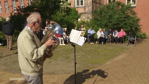 Peter Voß spielt auf seinem Blasinstrument im Hof des Augustenstifts vor einer Gruppe Senioren © Screenshot 