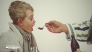 Gemälde, auf dem zu sehen ist, wie einem blonden Jungen von einem Erwachsenen ein Löffel mit Medizin vor den Mund gehalten wird. © Screenshot 