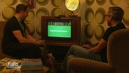 In einem Wohnzimmer im 1970er-Jahre-Stil spielen zwei Männer ein Tennis-Videospiel © Screenshot 
