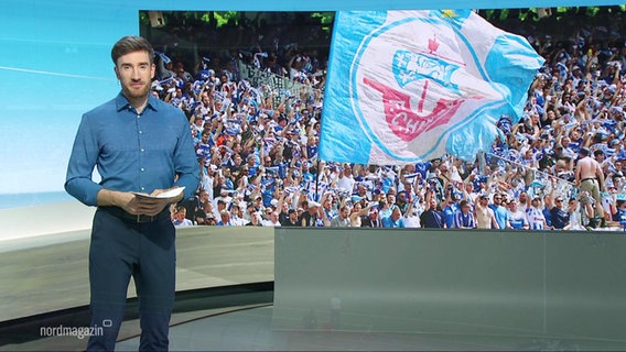 Der Moderator Stefan Leyh, im Hintergrund ein Bild von jubelnden Hansa Rostock Fans. © Screenshot 
