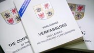 Drei kleine Bücher mit dem Titel "Vorläufige Verfassung" und dem Wappen von Mecklenburg-Vorpommern liegen auf einem Tisch. © Screenshot 