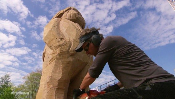 Ein Holzbildhauer arbeitet an einer Statue in Form eines bärtigen Mannes. © Screenshot 
