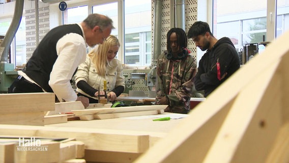 Ein Zimmermann zeigt drei jungen Menschen sein Handwerk. © Screenshot 