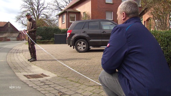 Zwei Männer vermessen eine Hauseinfahrt mit einem Metermaß. © Screenshot 
